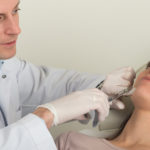 Auf dem Bild ist ein Facharzt zu sehen, der eine Faltenunterspritzung in Wien Dermacare bei einer Patientin durchführt. Der Arzt injiziert einen Filler, vermutlich Hyaluronsäure oder Radiesse, in den Gesichtsbereich der Patientin, während sie entspannt auf einer Behandlungsliege liegt. Der Einsatz von hochwertigen Faltenfillern wie Hyaluronsäure oder Radiesse ist eine effektive, minimalinvasive Methode, um das Hautbild zu verjüngen, Falten zu glätten und das Volumen wiederherzustellen. Die professionelle und präzise Anwendung dieser Filler durch erfahrene Ärzte, wie im Dermacare Institut, sorgt für natürliche, langanhaltende Ergebnisse, die die individuelle Schönheit der Patientin betonen.